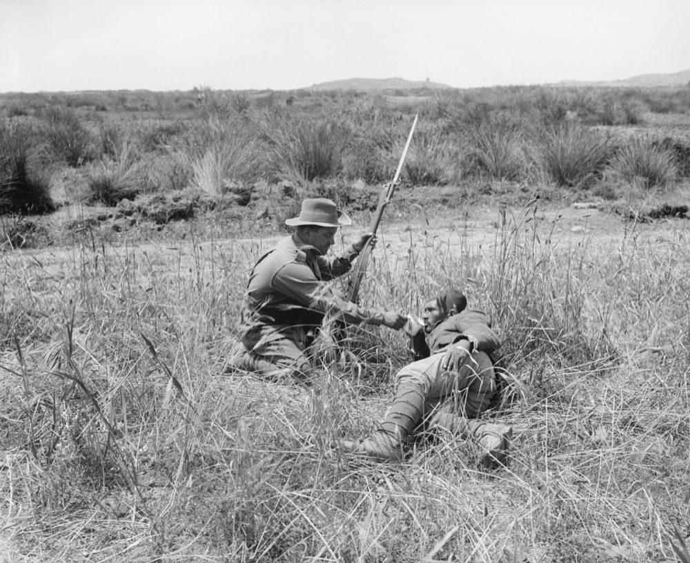 An Australian infantryman gives a drink to a wounded Turkish soldier. Achi Baba is the hill visible in the background. 